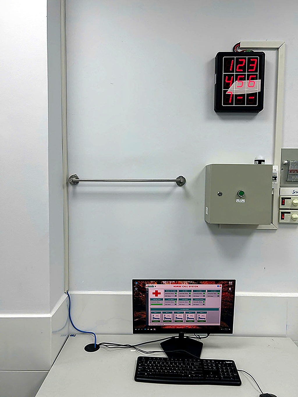 Control panel with digital display and computer setup on a white wall.