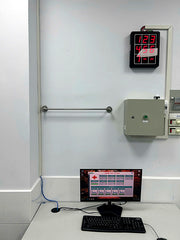 Control panel with digital display and computer setup on a white wall.