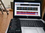 Laptop displaying an application with a smartphone showing text on a carpeted floor.