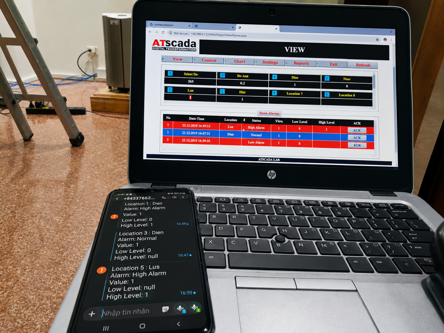 Laptop displaying an application with a smartphone showing text on a carpeted floor.