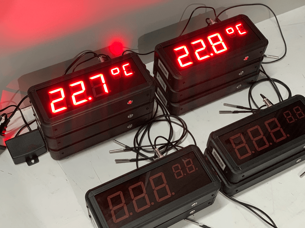 Digital temperature displays with red LED readings on a white surface.