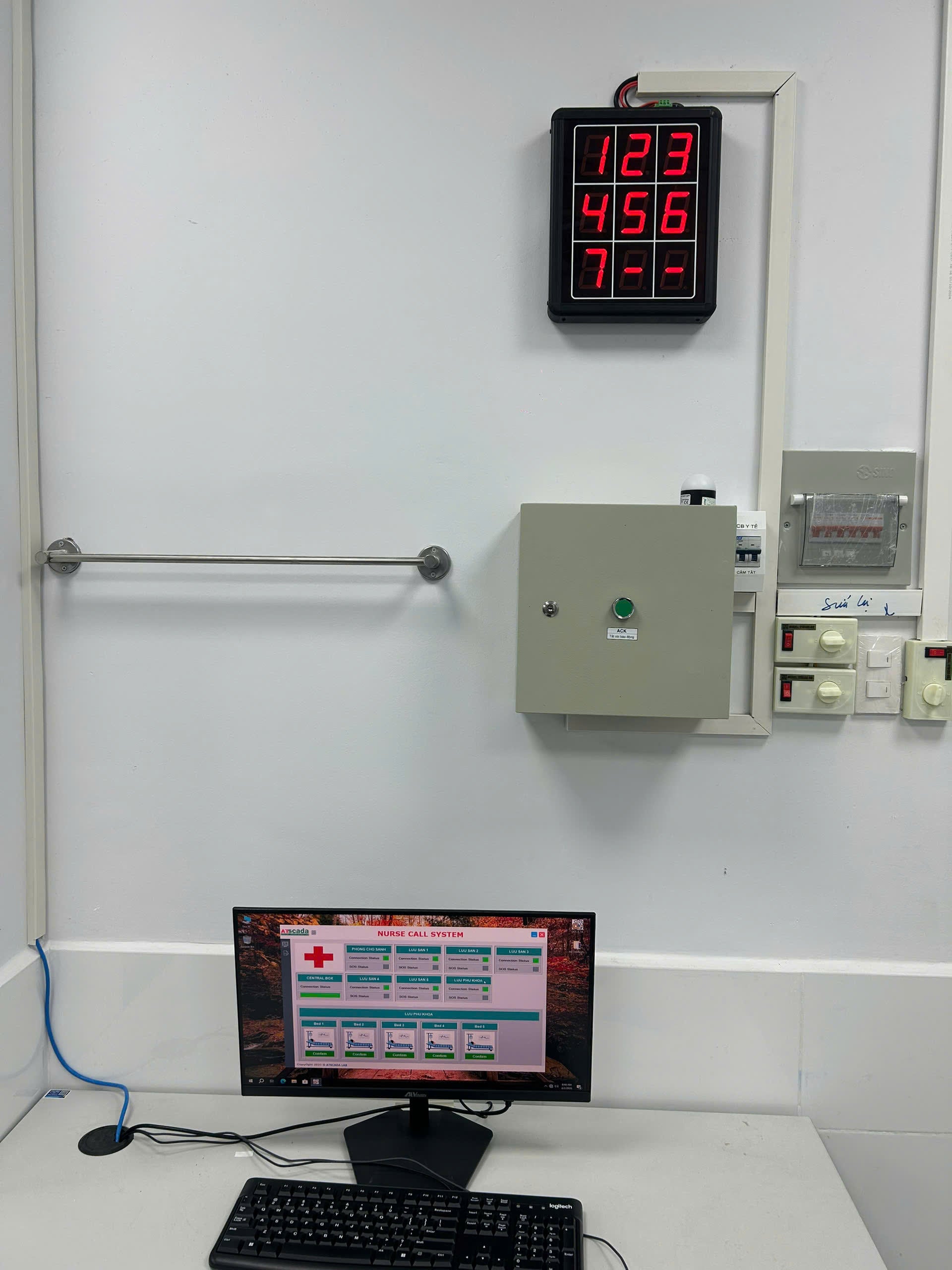 Control panel with digital display and computer setup on a white wall.