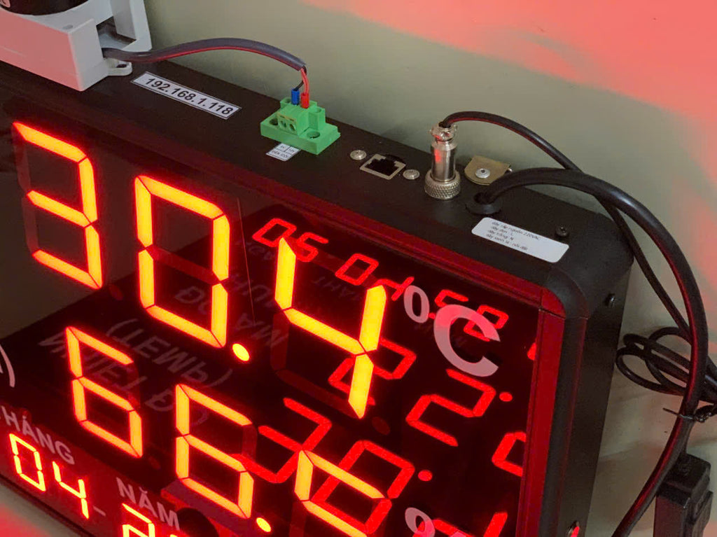 Digital clock with red LED display showing temperature and time on a blurred background